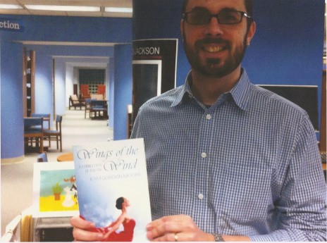 Ross White holding a copy of Wings of the Wind: A Cornucopia of Poetry donated by Kym Gordon Moore